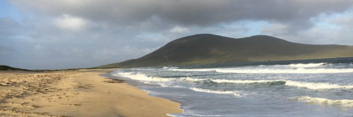 Waves breaking on a wide sandy beach with a hill rising behind it